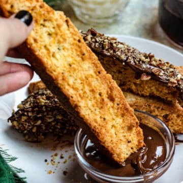 A hand dipping biscotti in melted chocolate.