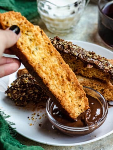 A hand dipping biscotti in melted chocolate.