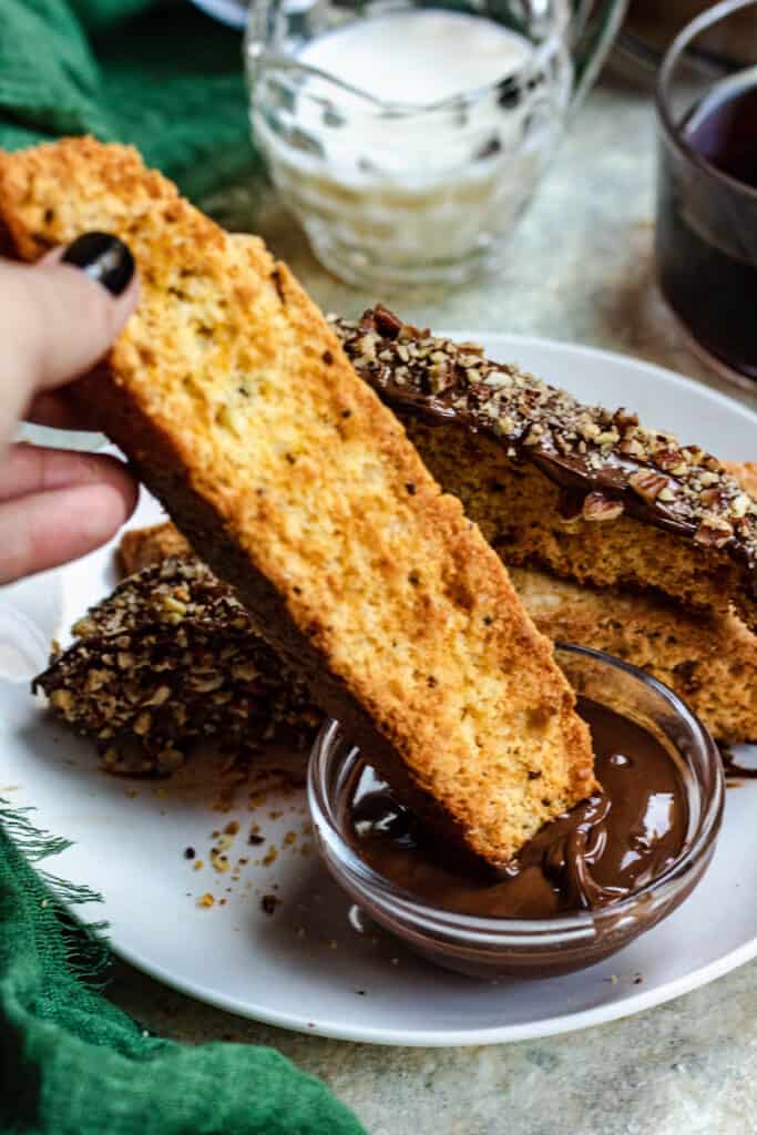 Hand holding biscotti cookie and dipping it in a small bowl of chocolate