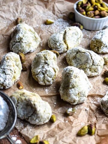 Pistachio cookies on a piece of parchment paper with pistachios surrounding them.