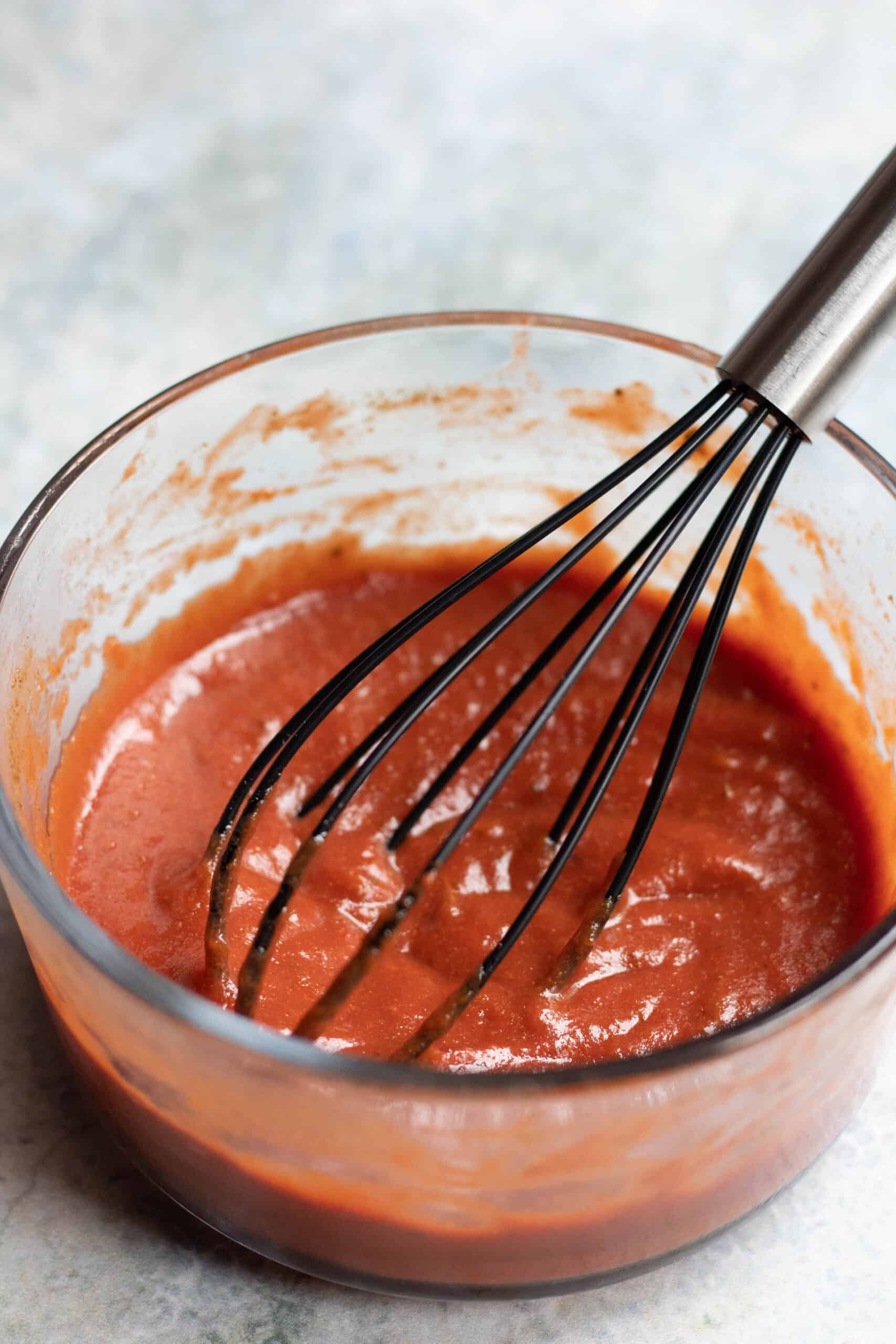 Pizza sauce with a whisk stirring in it. 