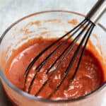 Pizza sauce in a glass bowl being whisked by a rubber whisk.