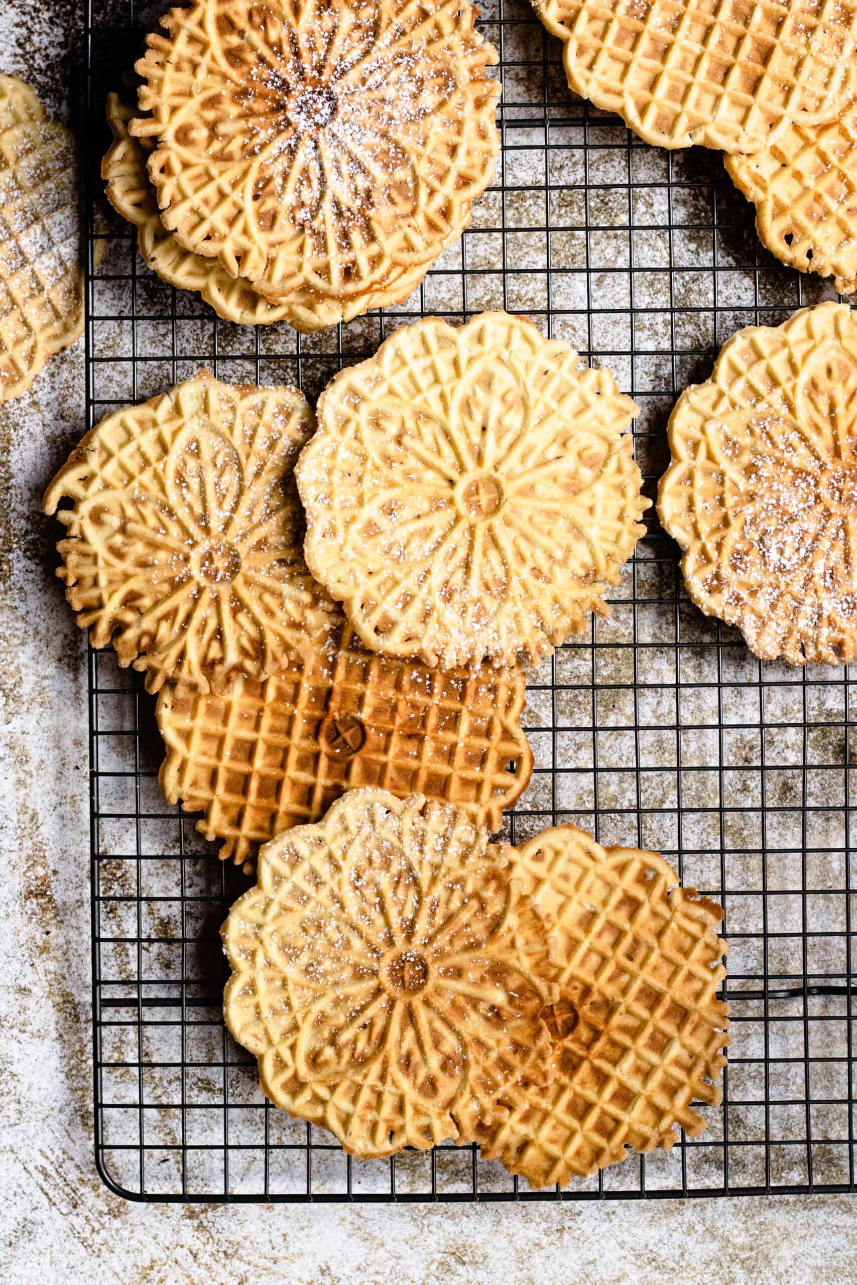 Pizzelles, Italian dessert recipe, laying on wire rack, some dusted with powdered sugar.