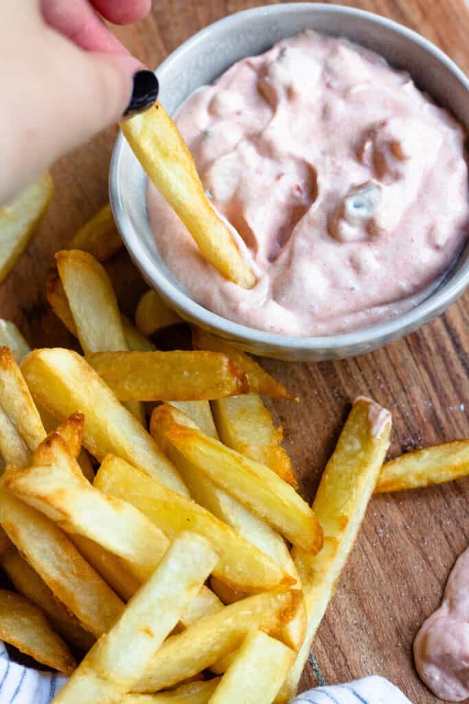 Hand dipping a Belgian fry in a pink andalouse sauce