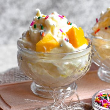 Espumillas in an ice cream cup with sprinkles and mangos on top.