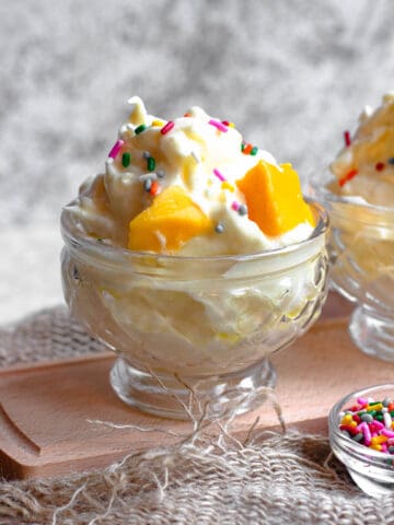 Espumillas in an ice cream cup with sprinkles and mangos on top.