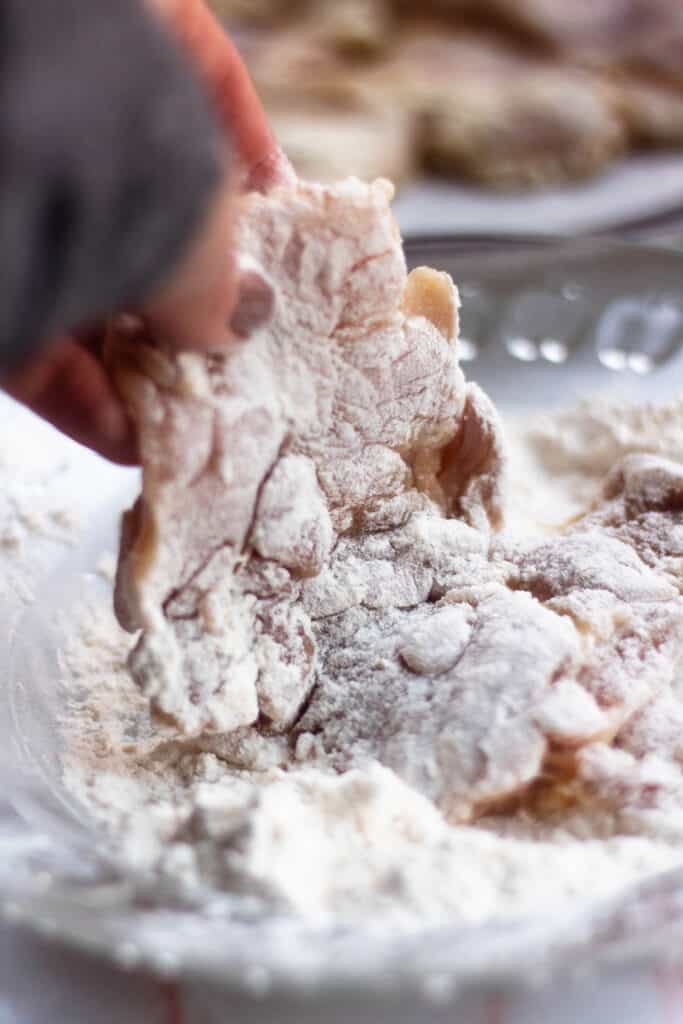 Hand dipping chicken in flour