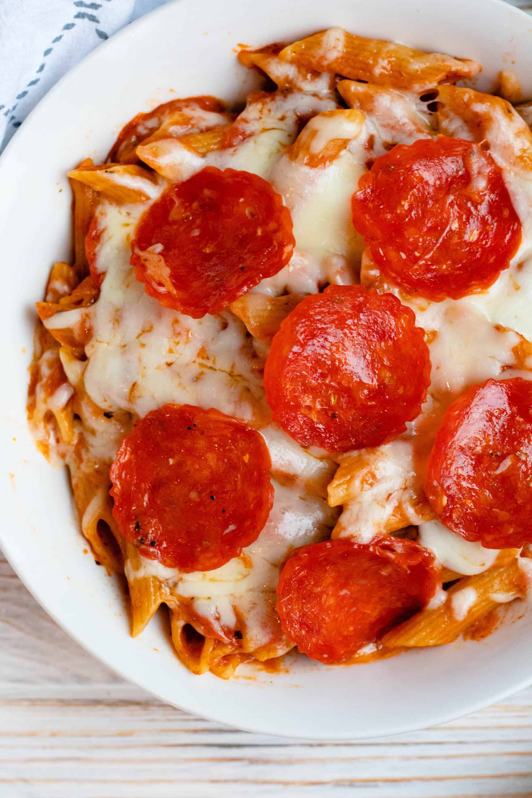 Pizza Pasta Bake in a white bowl topped with cheese and pepperoni.