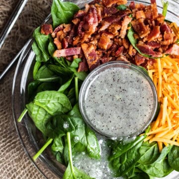 Spinach salad topped with bacon, cheese, and poppyseed dressing.