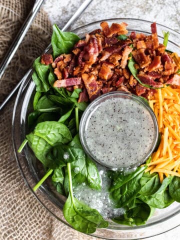 Spinach salad topped with bacon, cheese, and poppyseed dressing.