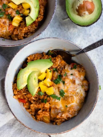 A bowl of bell pepper casserole topped with melted cheese, slices of avocado, and chopped yellow bell pepper.