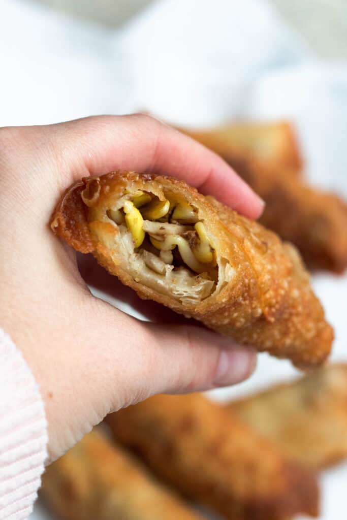 A hand holding an egg roll with a bite out of it, showing the interior. 