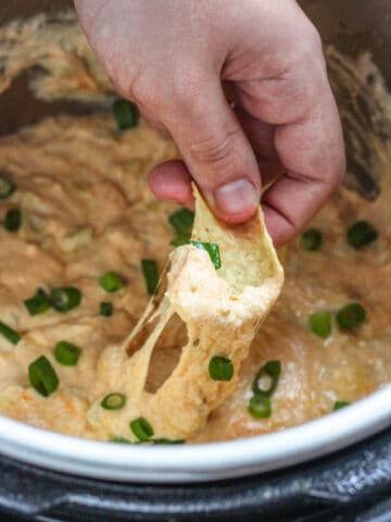 A hand using a chip to dip hot artichoke dip in the instant pot.