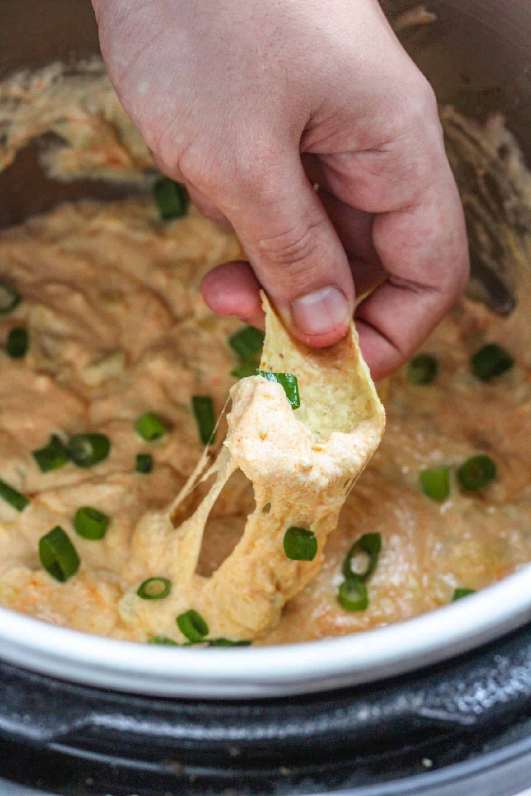 A hand using a chip to dip hot artichoke dip in the instant pot.