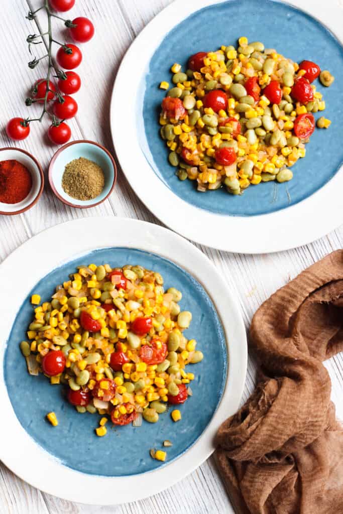 2 plates of succotash with tomatoes on a vine and 2 bowls of spices