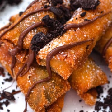 Oreo egg rolls in a pile with melted chocolate on top of them and crushed oreos surrounding them.