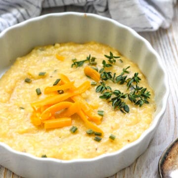 A small serving of polenta in a white dish topped with cheese and herbs.