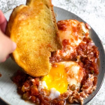 A hand dipping some bread in salsa eggs.