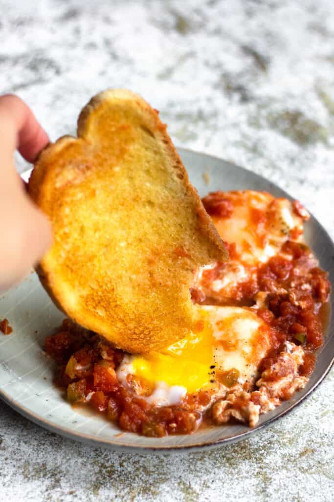 Piece of bread being dipping in eggs with salsa