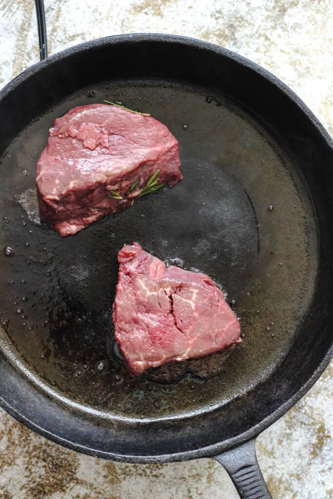 cast iron skillet with raw filet steaks