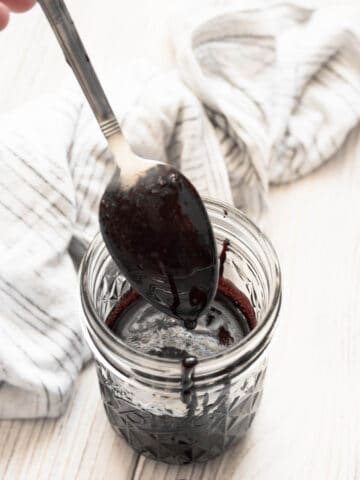 A spoon scooping out Balsamic Glaze from a glass jar.
