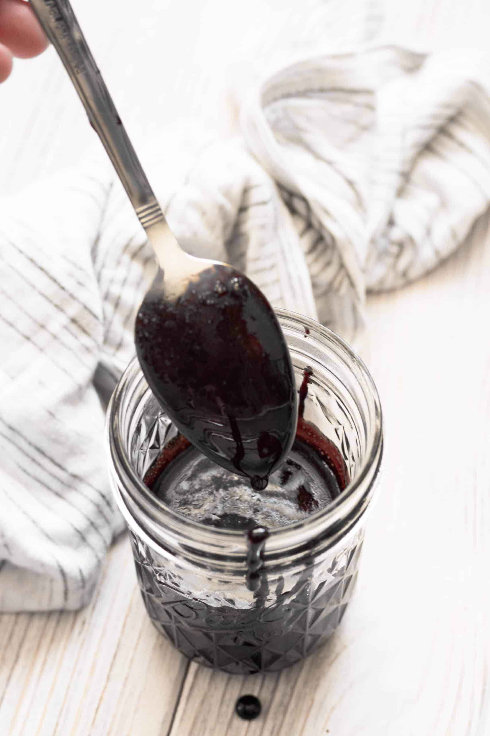 Spoon lifting out of a small glass jar coated with balsamic glaze. 
