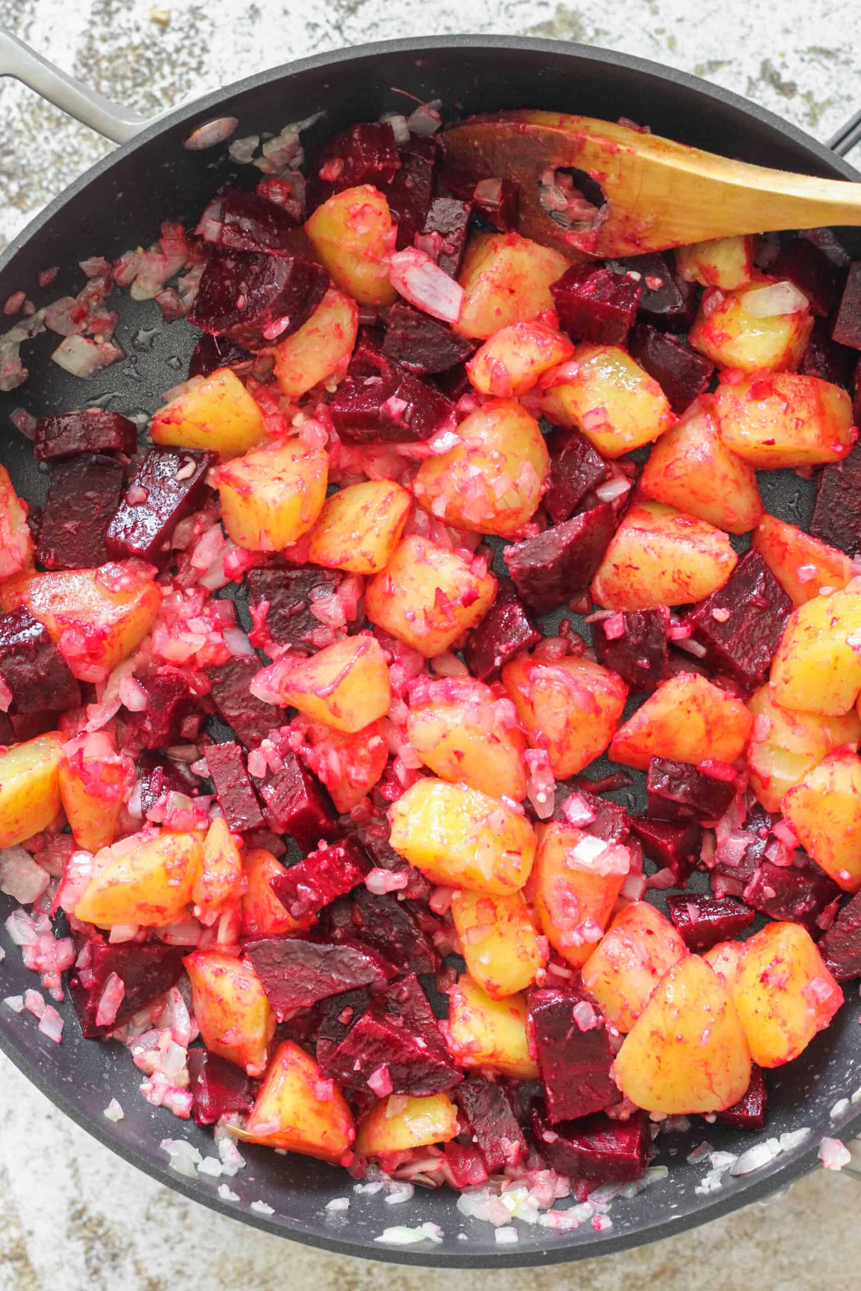Beet and Potato salad in a large pan with a wooden spoon.