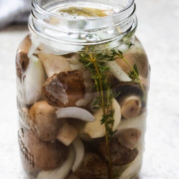 Pickled mushrooms in a jar with onions and thyme.