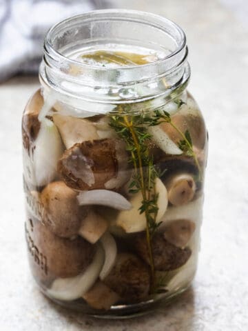 Pickled mushrooms in a jar with onions and thyme.