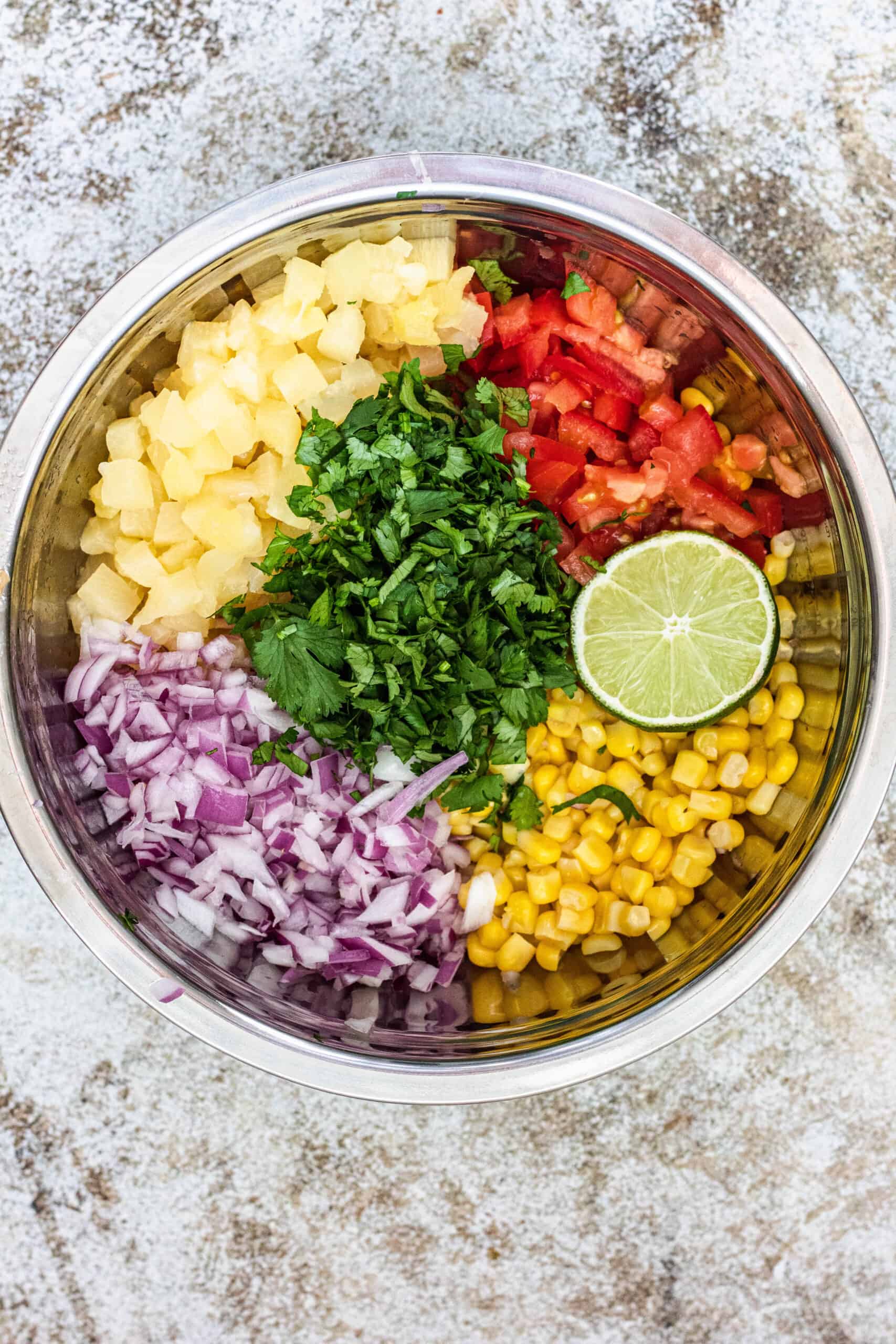 Pineapple corn salsa in a large mixing bowl with red onions, tomatoes, limes, and cilantro.