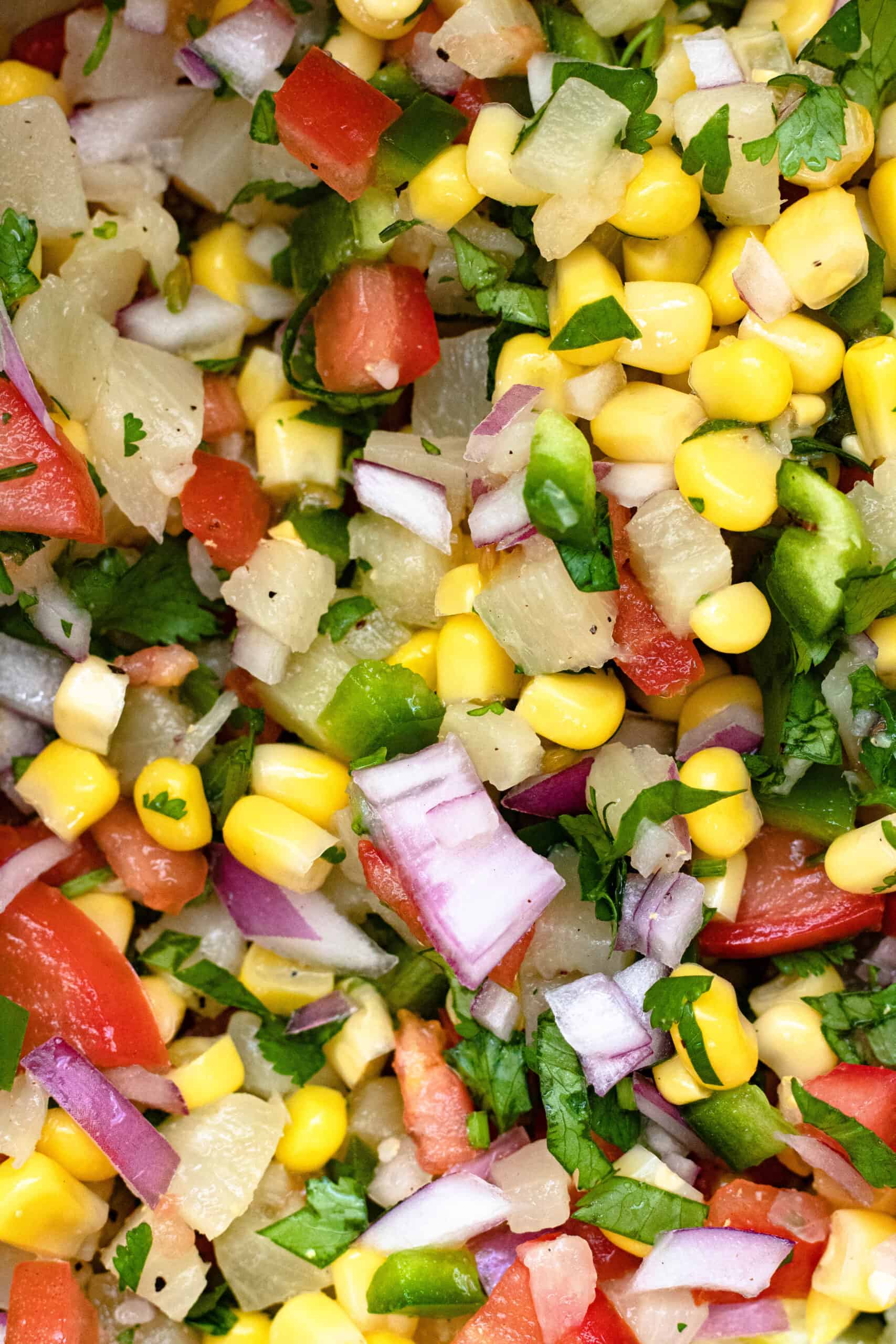 a close up of pineapple and corn salsa in a mixing bowl. 