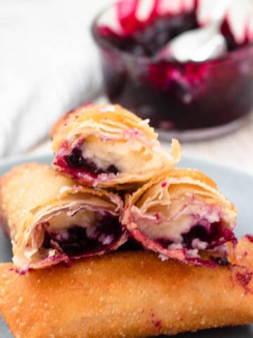 Blueberry cheesecake eggrolls on a plate with some cut open showing the cross section.