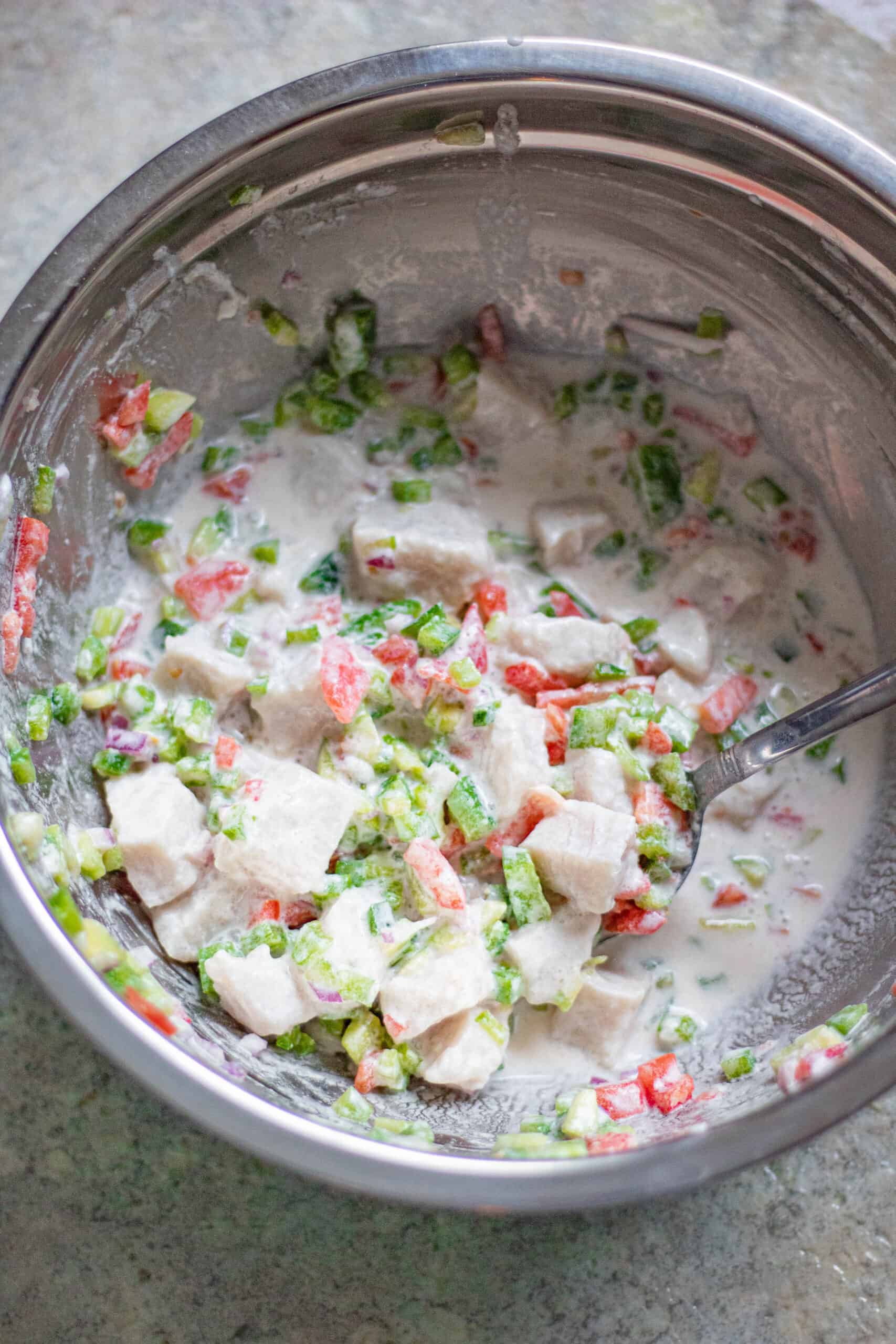Ceviche in a bowl being mixed with diced onions and tomatoes. 