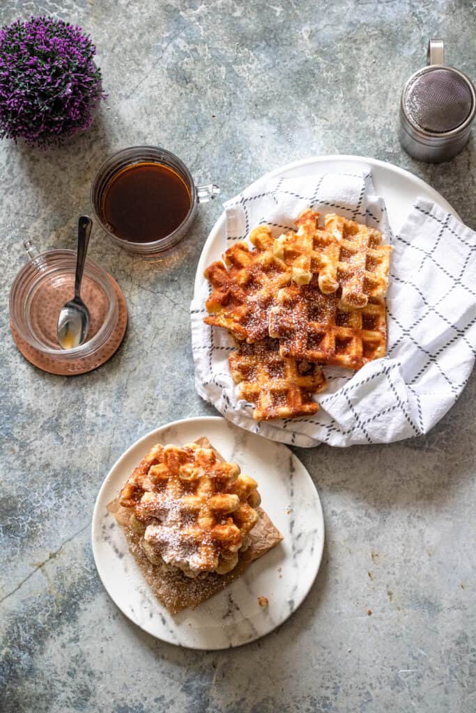 Liege waffles on a kitchen towel covered plate with a cup of coffee next to it. 