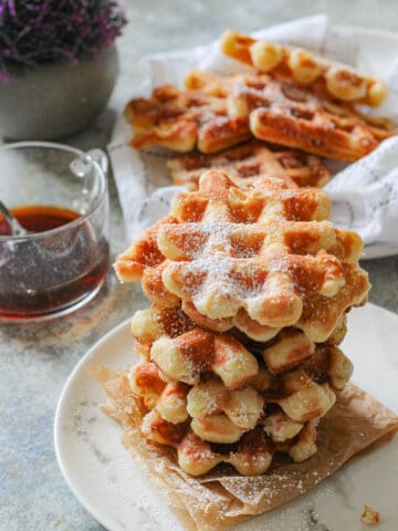 A pile of liege waffles on a plate, sprinkled with powdered sugar.