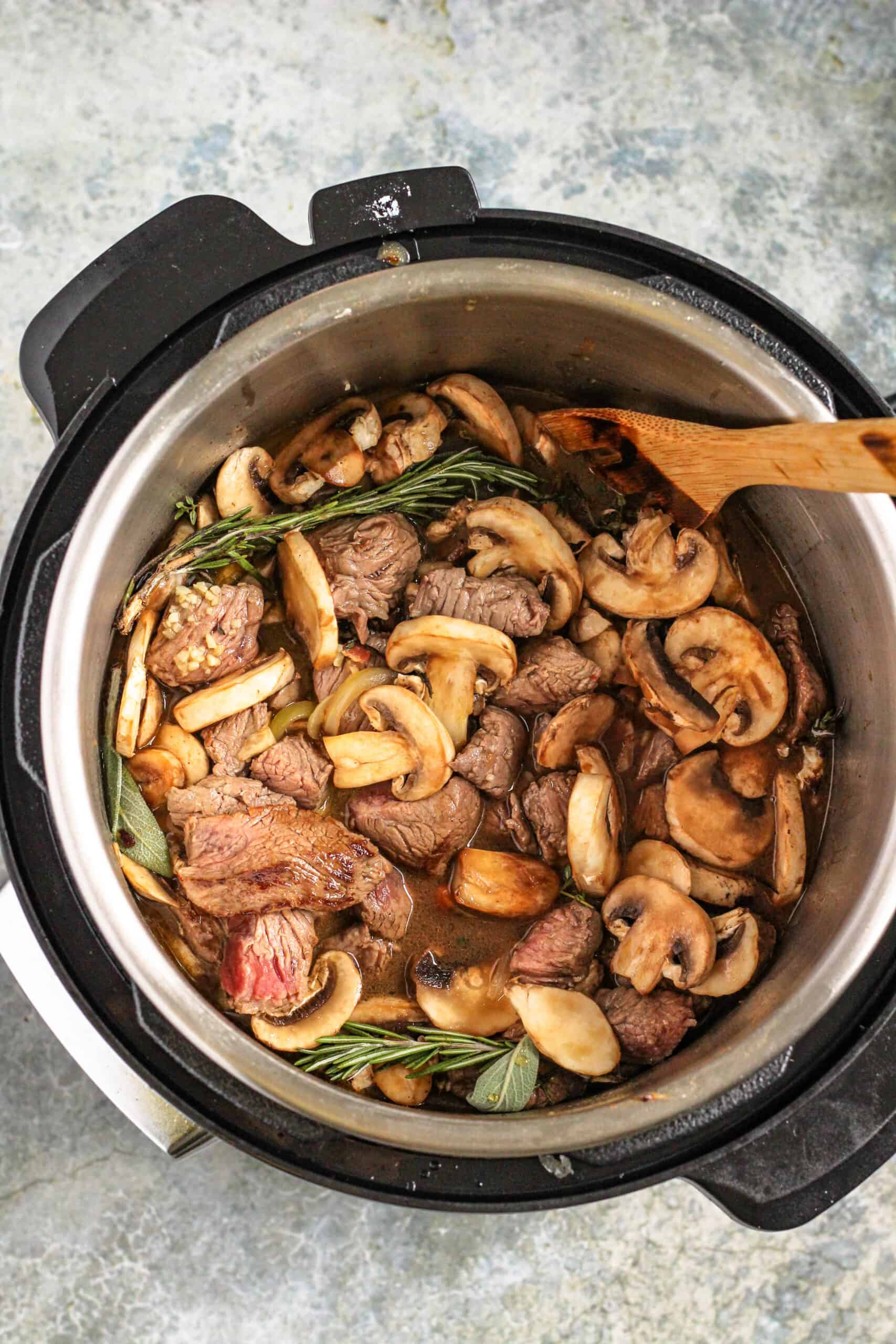 Beef chunks, mushrooms, garlic and fresh herbs sauted inside an instant pot ready to cook. 