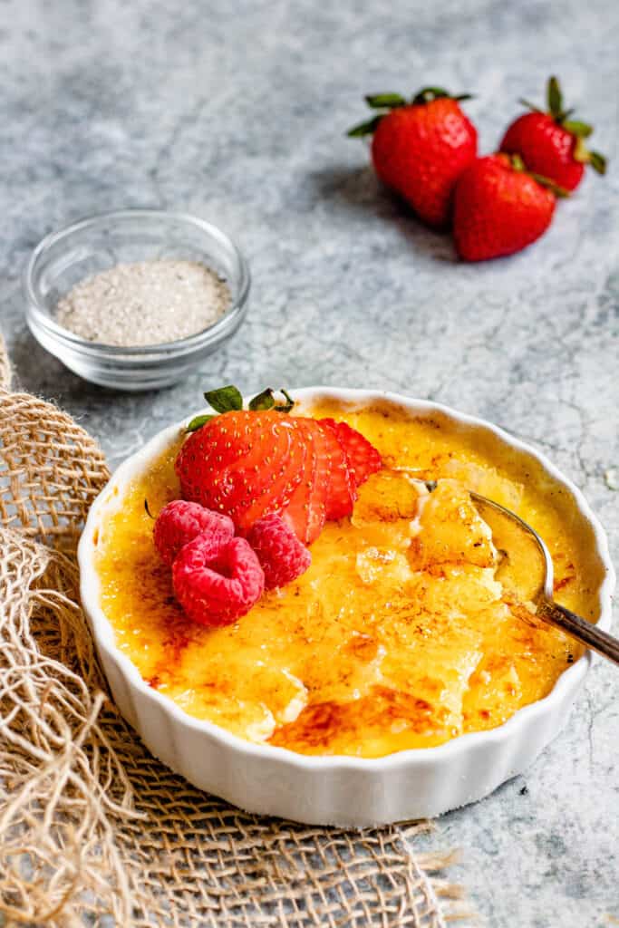 Front view of creme brulee with strawberries and raspberries and a cracked top with a spoon 
