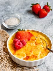 A scalloped bowl holding creme brulee with custard in the bowl and raspberries and strawberries on top to decorate.