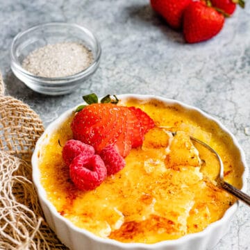 A scalloped bowl holding creme brulee with custard in the bowl and raspberries and strawberries on top to decorate.