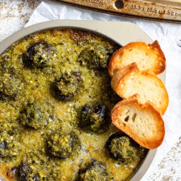 An escargot pan topped with escargot and served with baguette slices on the side.
