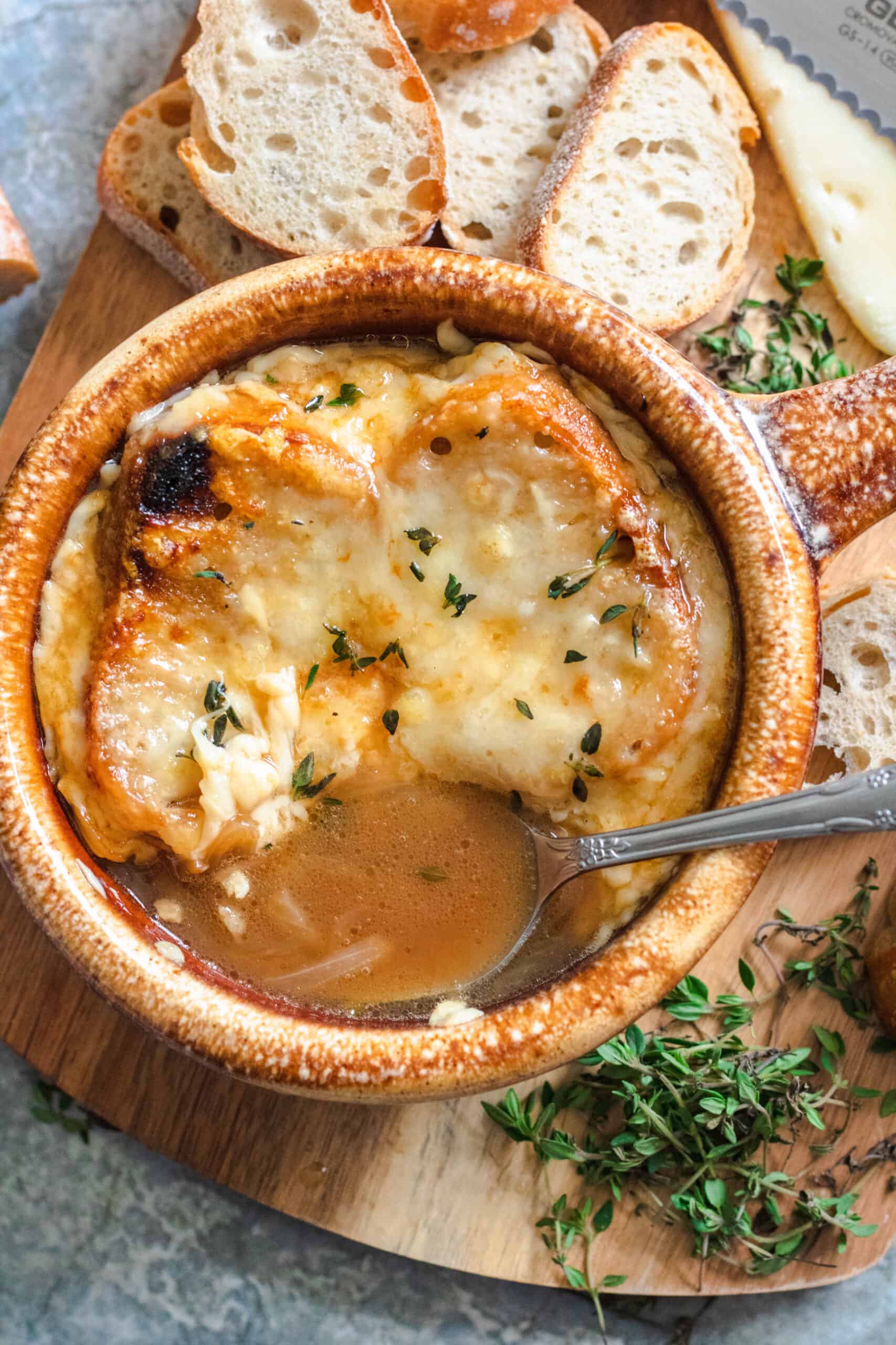 Spoon dipping into a bowl of french onion soup with melted cheese over a slice of bread. 