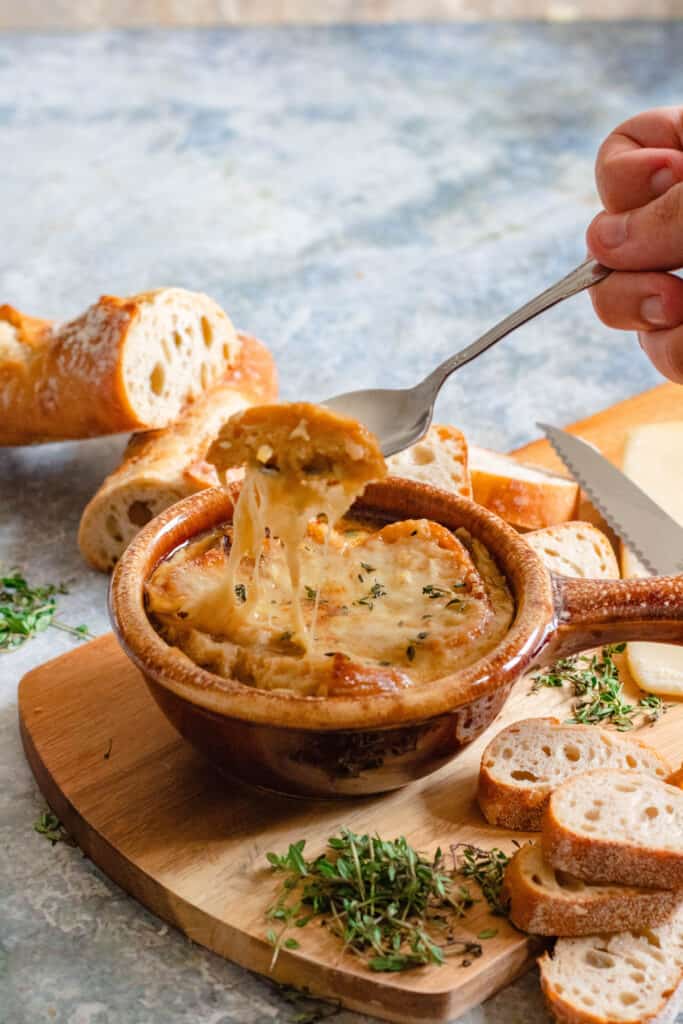 spoon scooping a bite of french onion soup with a cheese pull 