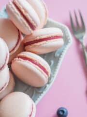 Pink macarons on a serving platter next to a large fork.