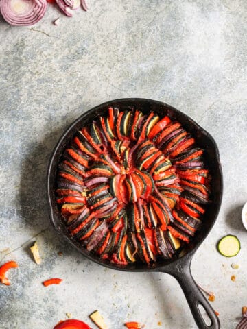 Ratatouille in a cast iron skillet with cut up ingredients scattered around it.