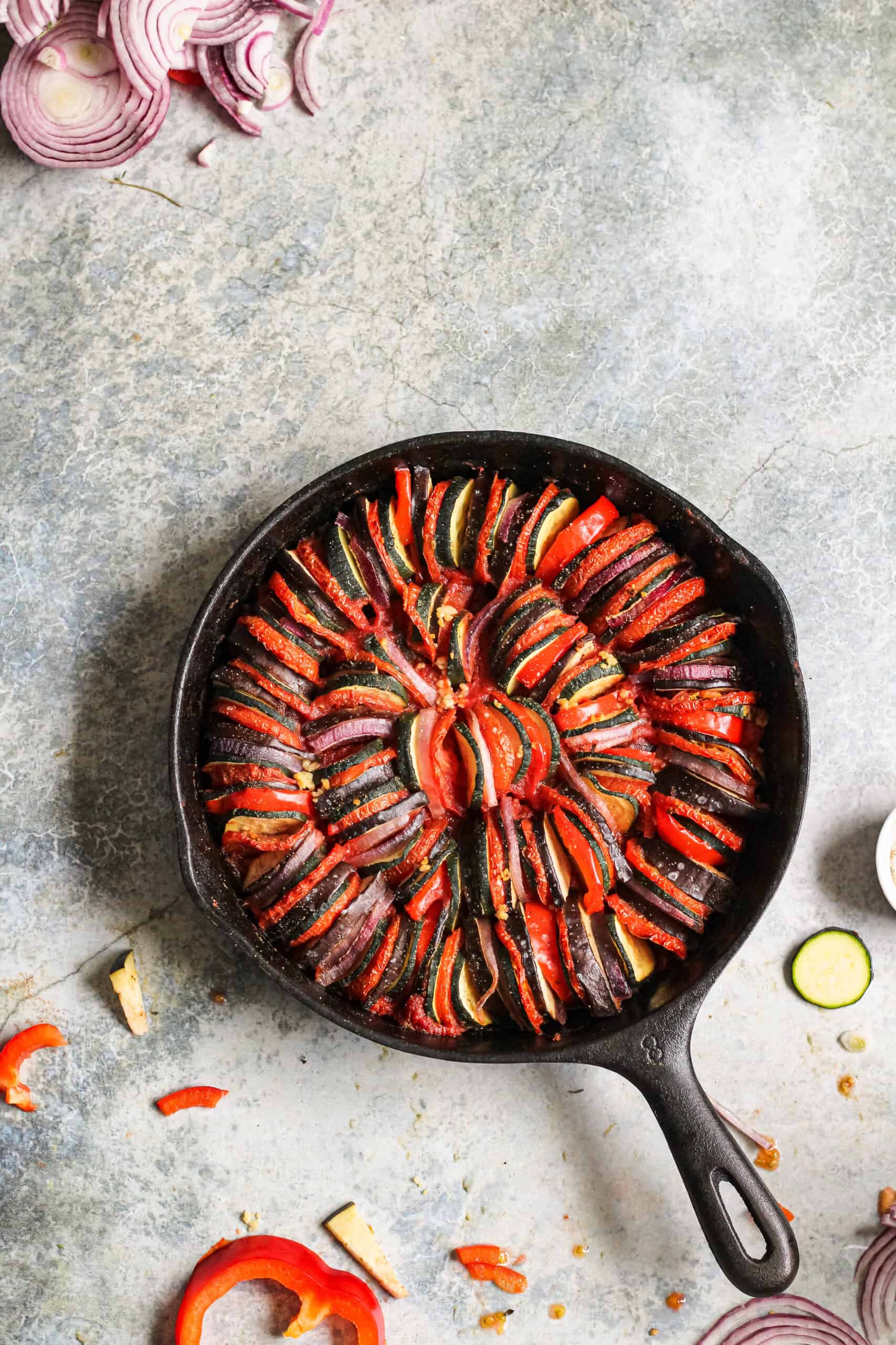Ratatouille in a cast iron skillet surrounded by chopped ingredients.