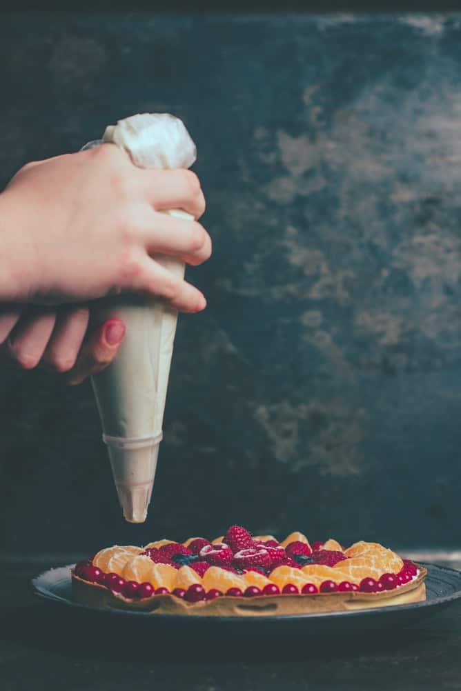 a hand piping cream onto a tart