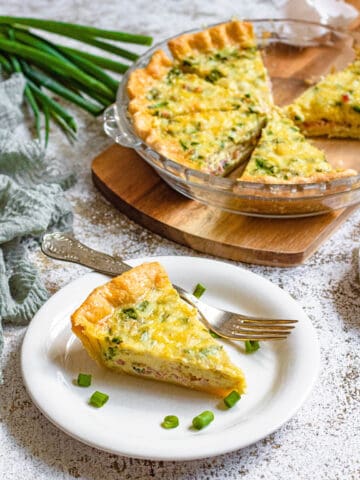 A slice of quiche on a plate surrounded by cut up green onions.