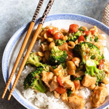 A bowl of cashew chicken with rice next to it and chopsticks on the side.