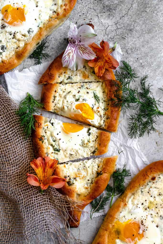 khachapuri cut into slices surrounded by herbs and flowers