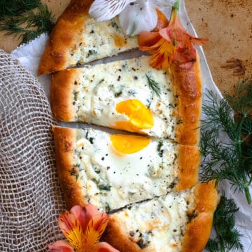 A khachapuri bread boat filled with herbed cheese and an egg, cut into slices.